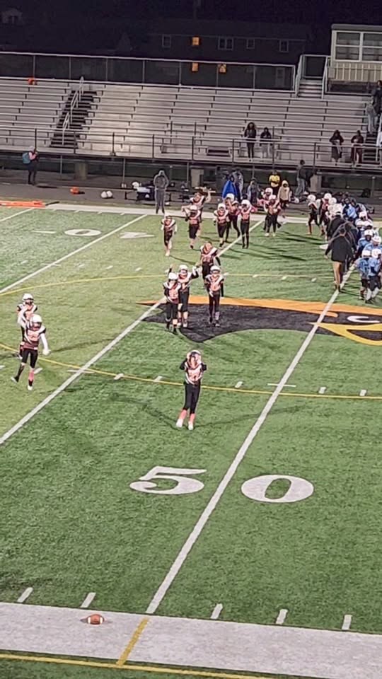 Little Eagle players and families on the field at night near the 50-yard line.